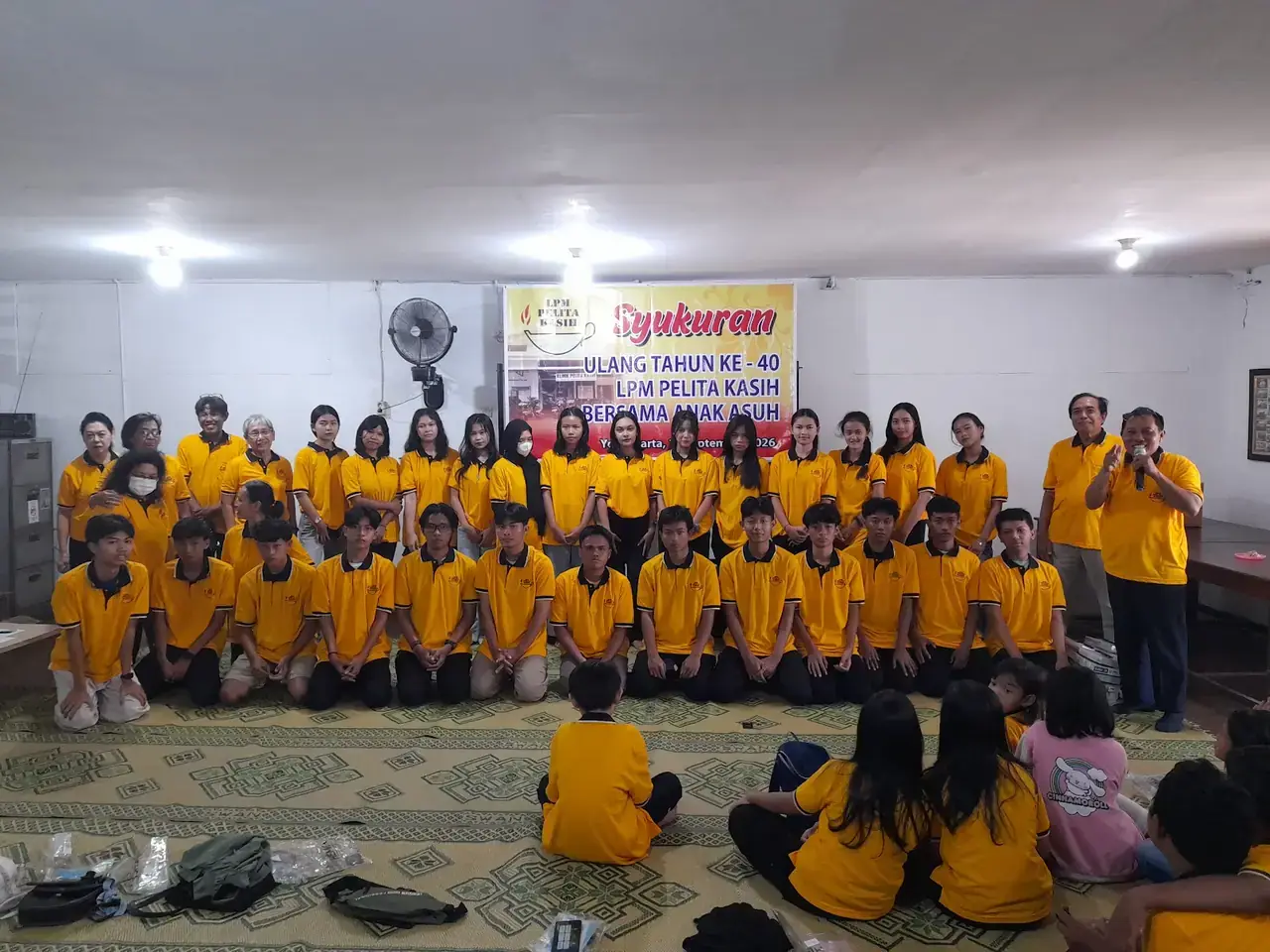Anak asuh berkaus kuning berfoto bersama di depan spanduk Syukuran Ulang Tahun ke-40 LPM Pelita Kasih